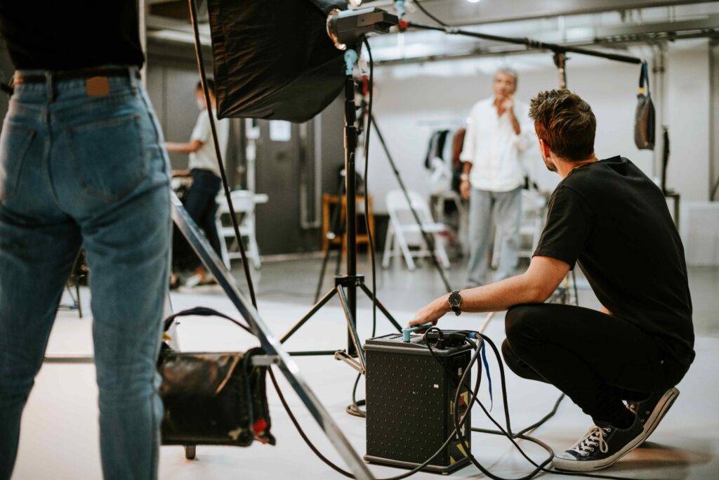 Techniker arbeitet an der Ausrüstung im gemieteten Fotostudio in Berlin, umgeben von professionellen Lichtern und Hintergrund, während ein Model im Hintergrund vorbereitet wird.