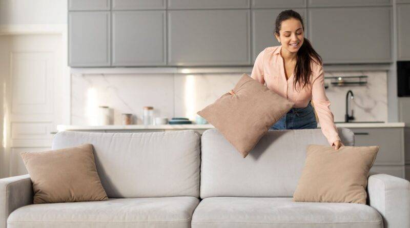 Glückliche Dame, die Kissen auf einer stilvollen Couch zu Hause arrangiert