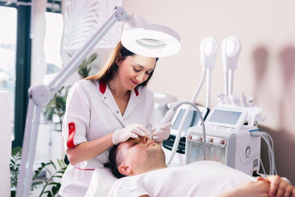 Kosmetikerin führt eine Hydrafacial Behandlung an einem Kunden durch in einem modernen Studio mit professionellen Geräten