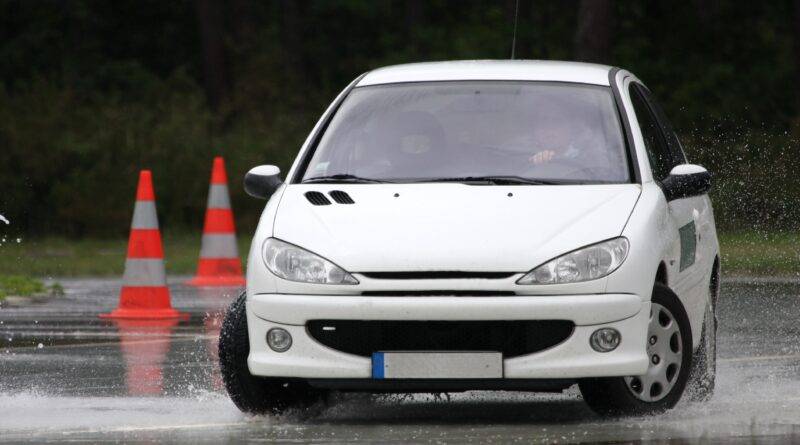 Ein weißes Auto absolviert eine Notbremsung auf nasser Fahrbahn beim Zwei-Phasen-Kurs Winterthur. Verkehrshütchen markieren die Strecke.