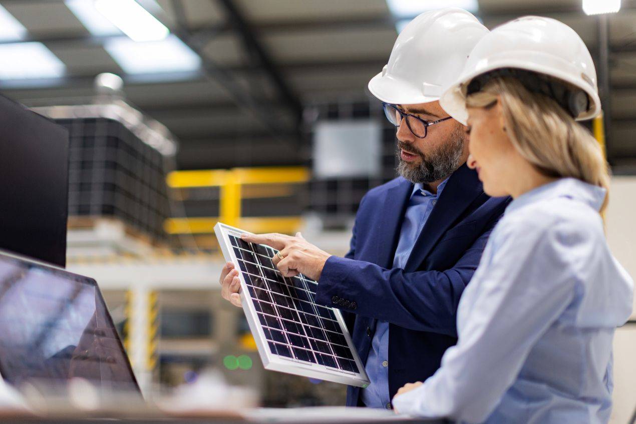 Zwei Ingenieure mit Schutzhelmen analysieren ein Solarmodul und besprechen die Integration des Sunny Tripower Smart Energy Systems