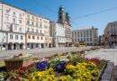 Linzer Hauptplatz mit historischen Häusern und bunten Blumenbeeten an einem sonnigen Frühlingstag