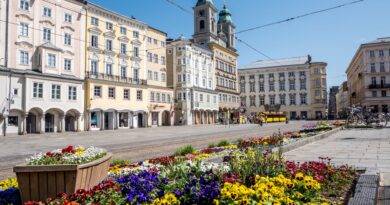 Linzer Hauptplatz mit historischen Häusern und bunten Blumenbeeten an einem sonnigen Frühlingstag