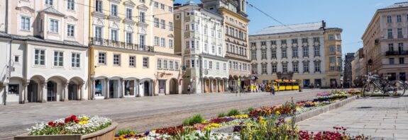 Linzer Hauptplatz mit historischen Häusern und bunten Blumenbeeten an einem sonnigen Frühlingstag