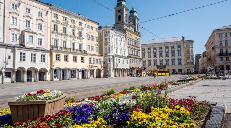 Linzer Hauptplatz mit historischen Häusern und bunten Blumenbeeten an einem sonnigen Frühlingstag