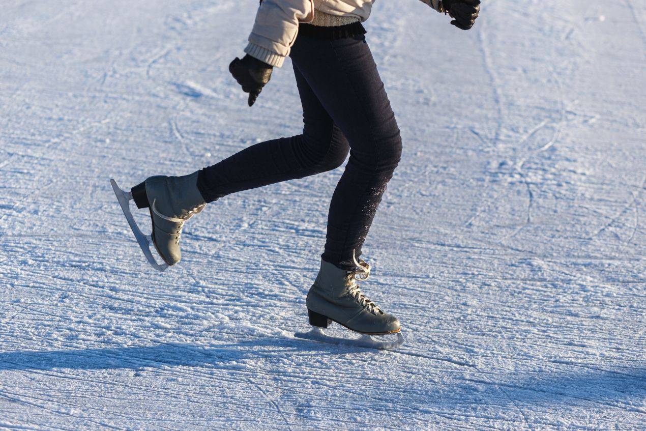 Person in Winterkleidung läuft mit Schlittschuhen über eine Eisfläche – Nahaufnahme der Beine in Bewegung auf dem Eis