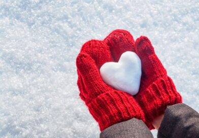 Zwei rote Handschuhe halten ein Herz aus Schnee – Symbol für Winterspaß und Aktivitäten mit Schlittschuhen im Freien