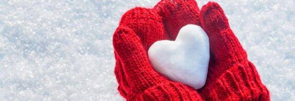 Zwei rote Handschuhe halten ein Herz aus Schnee – Symbol für Winterspaß und Aktivitäten mit Schlittschuhen im Freien
