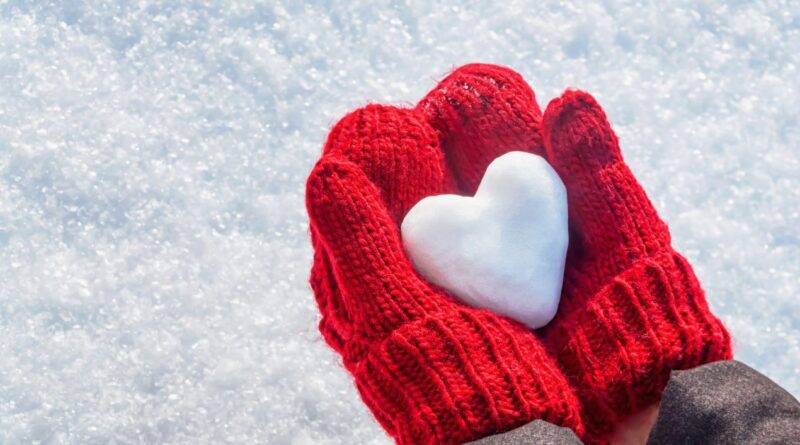 Zwei rote Handschuhe halten ein Herz aus Schnee – Symbol für Winterspaß und Aktivitäten mit Schlittschuhen im Freien