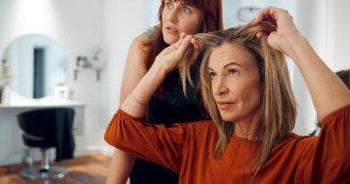 Frau im Friseursalon zeigt auf ihr feines Haar und erhält Beratung für mehr Volumen mit Extensions