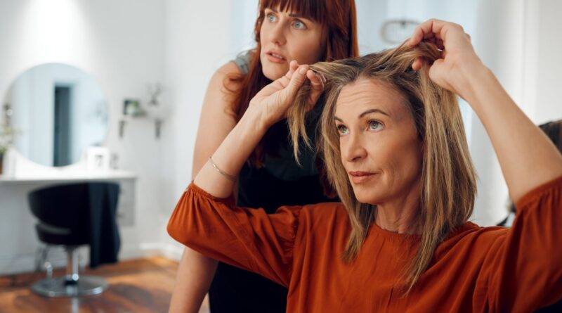 Frau im Friseursalon zeigt auf ihr feines Haar und erhält Beratung für mehr Volumen mit Extensions