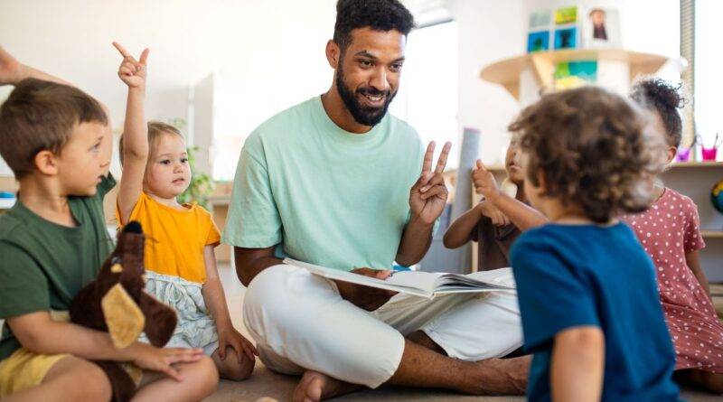 Erzieher sitzt mit Kindern im Kreis und liest vor – Symbolbild fuer Kita Assistenz und paedagogische Unterstuetzung im Kindergarten